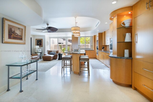 kitchen featuring ceiling fan, pendant lighting, a tray ceiling, a center island, and a kitchen bar