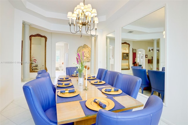 tiled dining room with a raised ceiling, a chandelier, and decorative columns