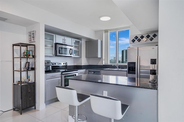 kitchen with light tile patterned flooring, sink, gray cabinetry, appliances with stainless steel finishes, and a breakfast bar area