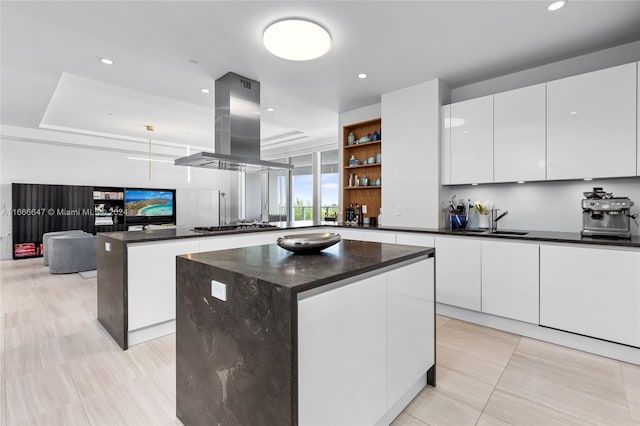 kitchen with island exhaust hood, a kitchen island, sink, and white cabinetry