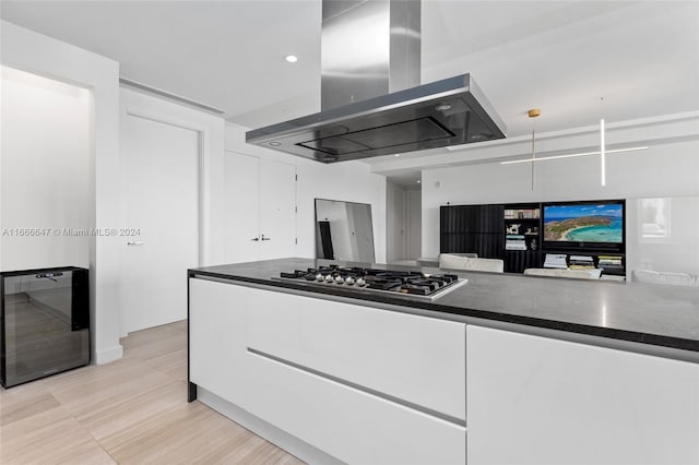 kitchen with island range hood, stainless steel gas cooktop, heating unit, and white cabinets