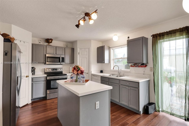 kitchen featuring dark wood-type flooring, stainless steel appliances, a textured ceiling, a center island, and sink