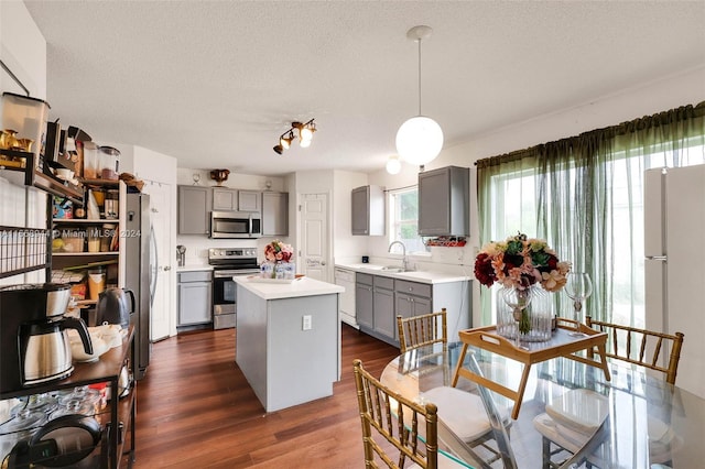 kitchen featuring a kitchen island, dark hardwood / wood-style flooring, gray cabinets, stainless steel appliances, and decorative light fixtures