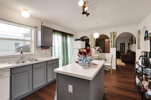 kitchen with a textured ceiling, a center island, dark hardwood / wood-style floors, hanging light fixtures, and white appliances