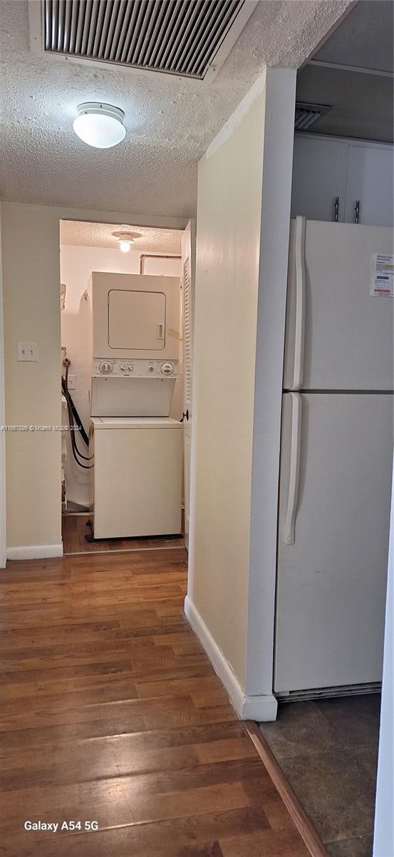 hall featuring stacked washer and dryer, hardwood / wood-style flooring, and a textured ceiling