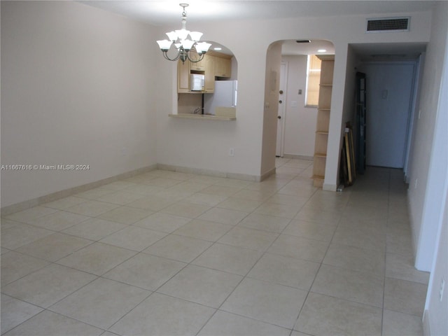 empty room with light tile patterned flooring and a chandelier