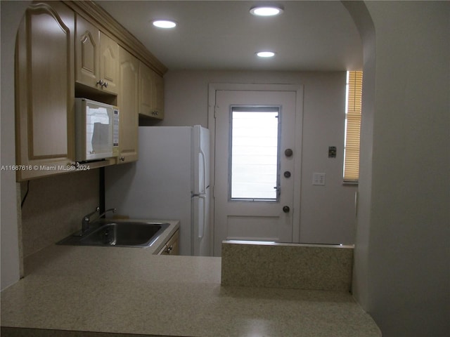 kitchen featuring white appliances, kitchen peninsula, light brown cabinets, and sink