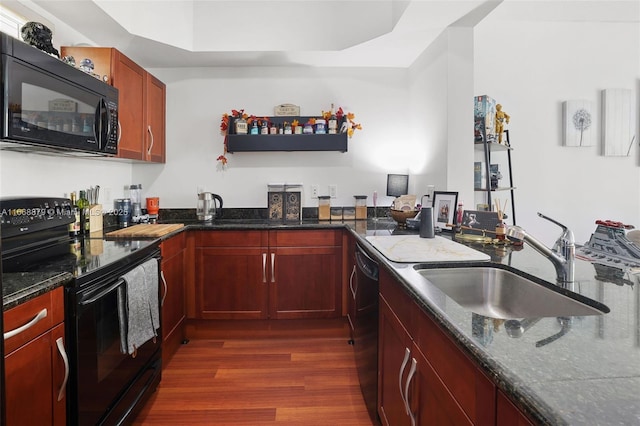 kitchen featuring a sink, dark wood-type flooring, dark stone counters, black appliances, and reddish brown cabinets