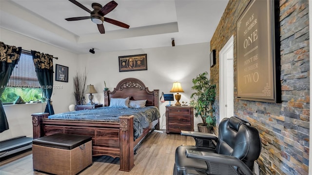 bedroom featuring ceiling fan, a raised ceiling, and light hardwood / wood-style floors