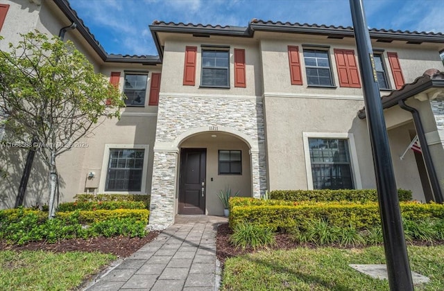 view of front facade featuring stone siding, a tile roof, and stucco siding