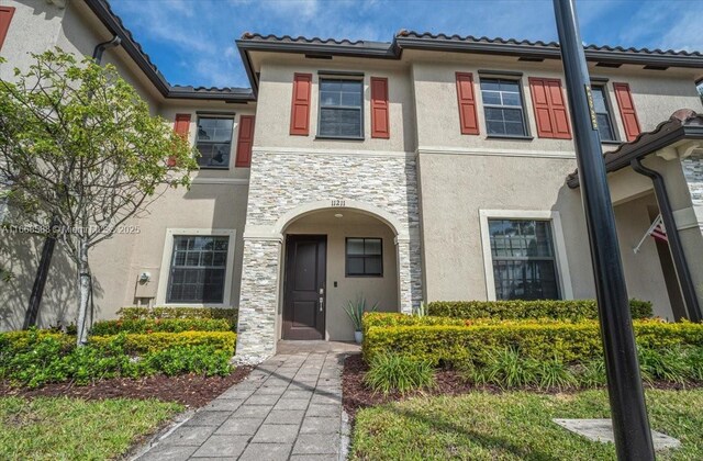 view of front facade featuring stone siding, a tile roof, and stucco siding