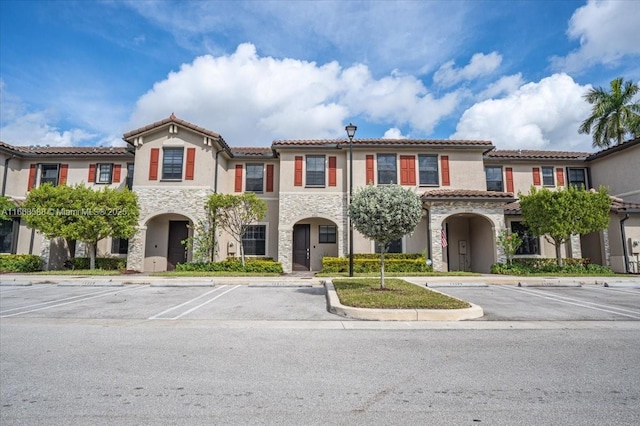 mediterranean / spanish-style home featuring uncovered parking, stone siding, and stucco siding