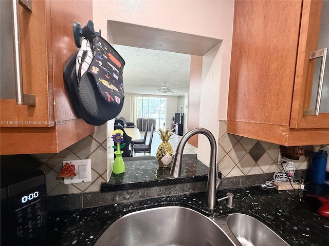 kitchen with a textured ceiling, tasteful backsplash, sink, dark stone countertops, and ceiling fan