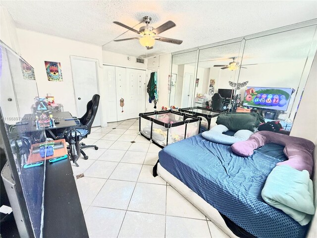 bedroom featuring ceiling fan, multiple closets, a textured ceiling, and light tile patterned floors