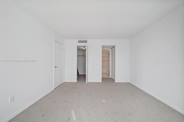 unfurnished bedroom with connected bathroom, a spacious closet, light colored carpet, and a textured ceiling