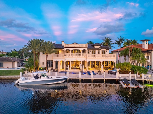 back house at dusk featuring a balcony and a water view