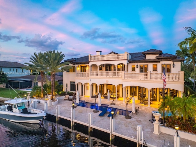 back house at dusk featuring a patio, a balcony, and a water view