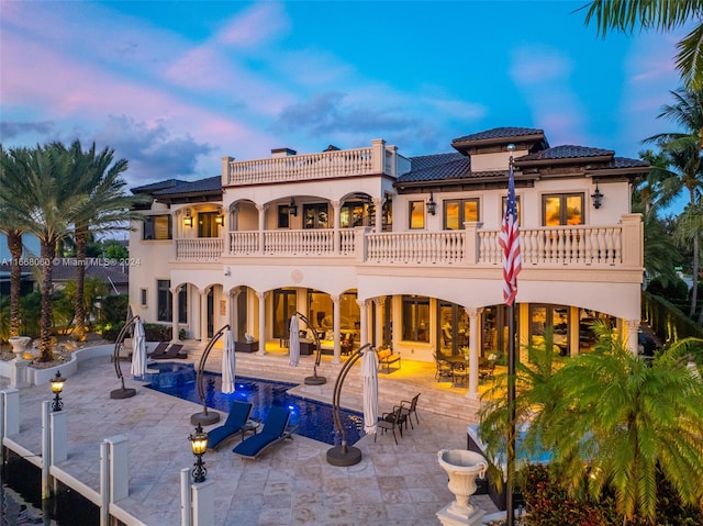 back house at dusk with a balcony and a patio area