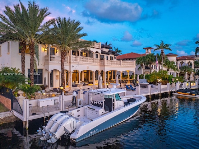 back house at dusk featuring a balcony, a water view, and a patio area