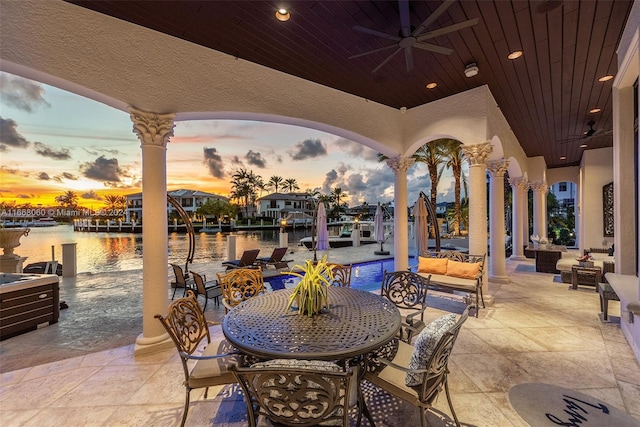 patio terrace at dusk with ceiling fan, an outdoor living space, and a water view