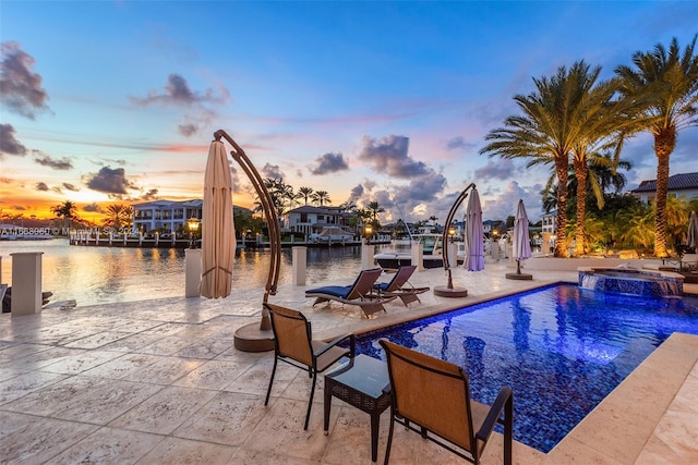 pool at dusk featuring a water view, an in ground hot tub, and a patio area