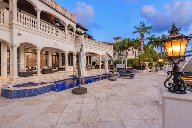 pool at dusk with pool water feature, a patio, an in ground hot tub, and outdoor lounge area