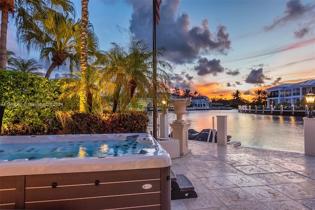 pool at dusk featuring a patio and a water view