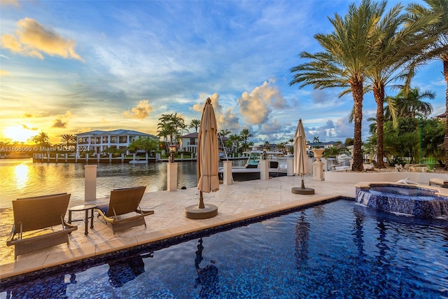 pool at dusk featuring a water view, a patio, and an in ground hot tub