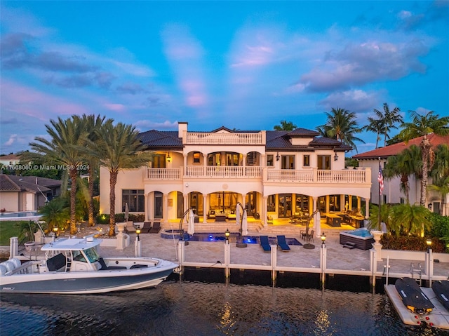 back house at dusk featuring a patio, a water view, and a balcony