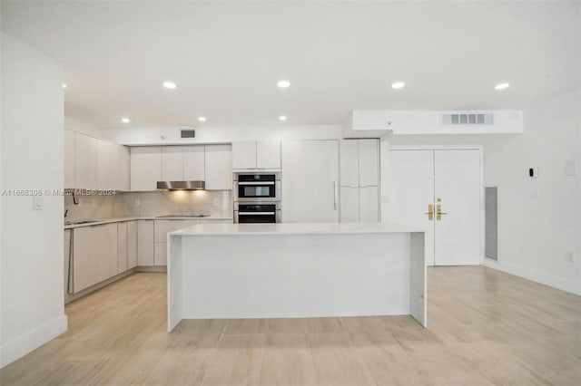 kitchen with light hardwood / wood-style floors, a kitchen island, stainless steel double oven, and white cabinetry