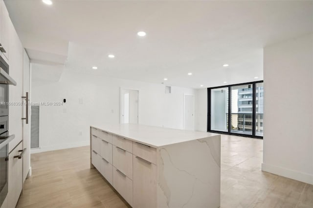 kitchen featuring light stone counters, expansive windows, a spacious island, and light hardwood / wood-style floors