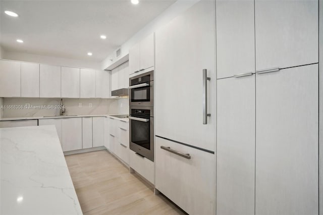 kitchen featuring backsplash, white cabinets, sink, light hardwood / wood-style flooring, and light stone countertops