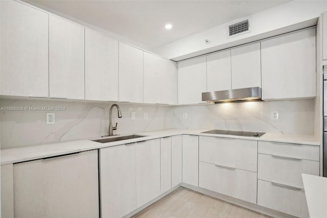 kitchen featuring white cabinetry, decorative backsplash, black cooktop, and sink