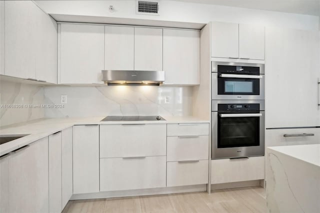 kitchen featuring decorative backsplash, light stone counters, black electric cooktop, double oven, and white cabinets