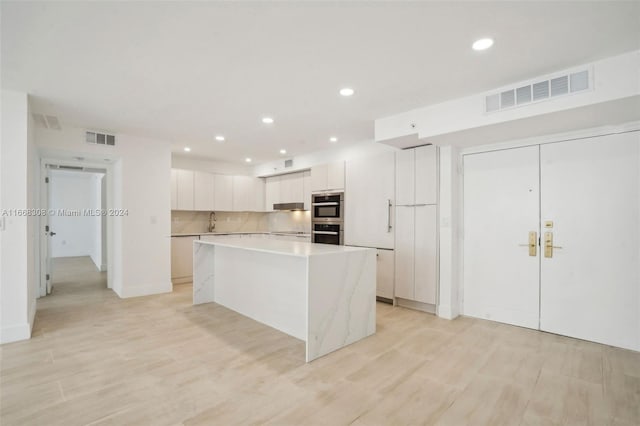 kitchen with stainless steel double oven, sink, light hardwood / wood-style flooring, white cabinets, and a large island