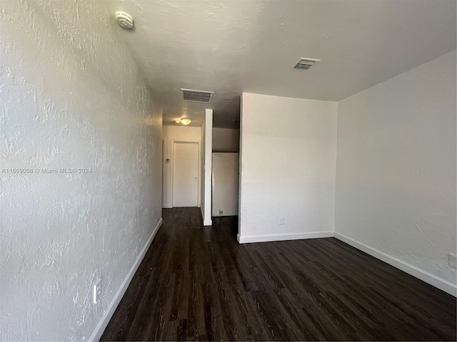empty room featuring dark wood-style flooring, baseboards, and visible vents
