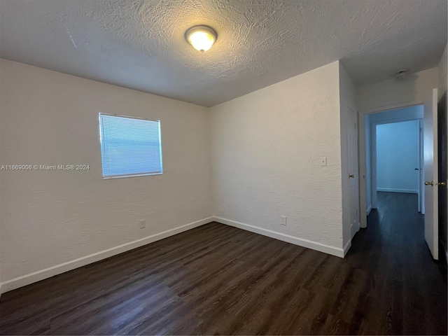 empty room with baseboards, a textured ceiling, dark wood-style flooring, and a textured wall