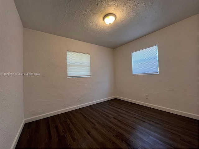 spare room with a textured ceiling, baseboards, dark wood finished floors, and a textured wall