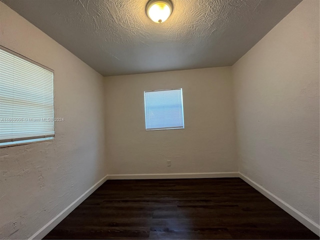 spare room featuring baseboards, dark wood-style flooring, and a healthy amount of sunlight