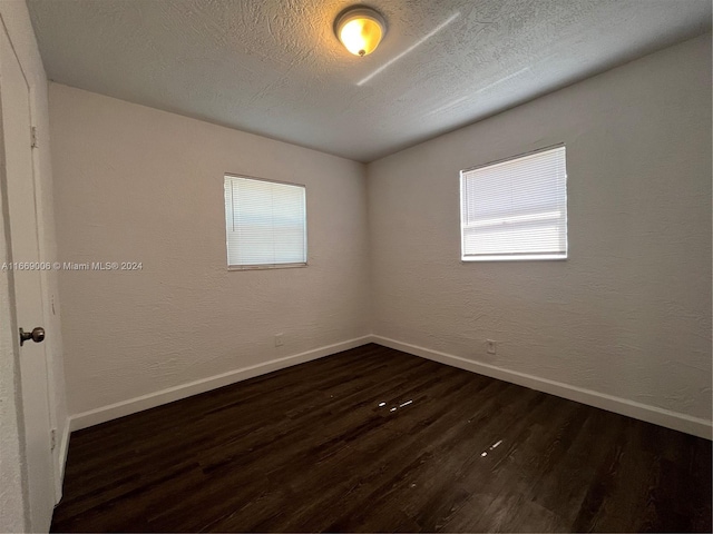 spare room with baseboards, a textured ceiling, dark wood finished floors, and a healthy amount of sunlight