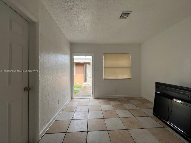 interior space featuring light tile patterned flooring, a textured wall, a textured ceiling, baseboards, and visible vents