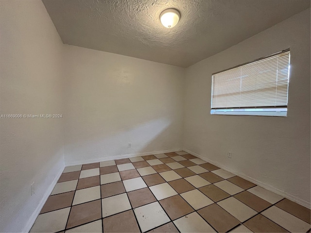 unfurnished room with baseboards and a textured ceiling