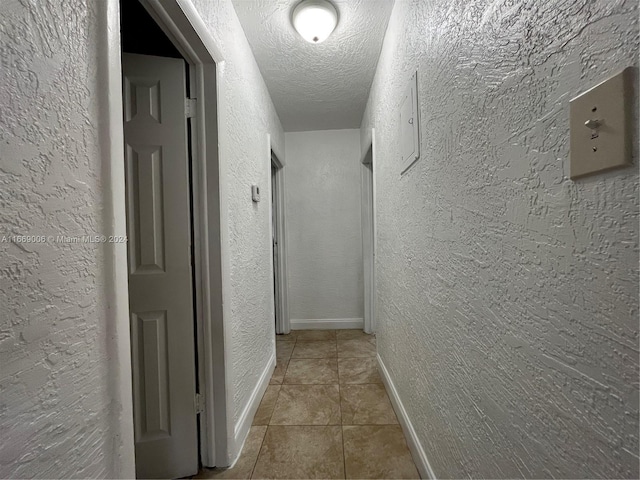 corridor with a textured ceiling, a textured wall, baseboards, and tile patterned flooring