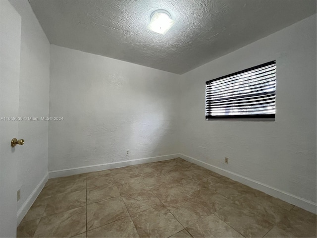 unfurnished room with baseboards and a textured ceiling