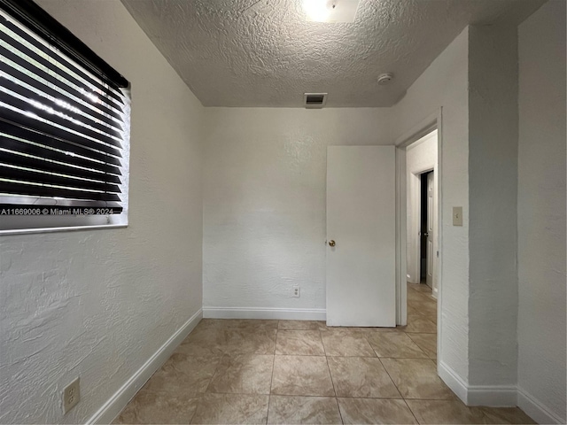 spare room with a textured ceiling, visible vents, light tile patterned floors, baseboards, and a textured wall