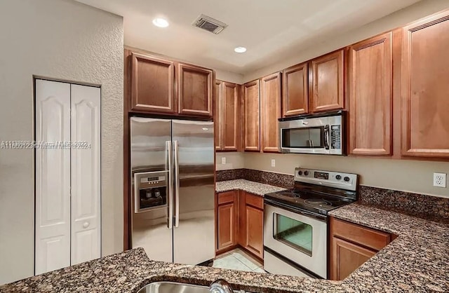 kitchen featuring stainless steel appliances, light tile patterned floors, and dark stone counters