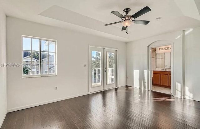 empty room with light hardwood / wood-style flooring, ceiling fan, a raised ceiling, and plenty of natural light