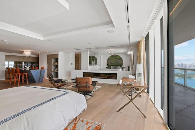 bedroom with a raised ceiling, light hardwood / wood-style floors, a water view, and ceiling fan