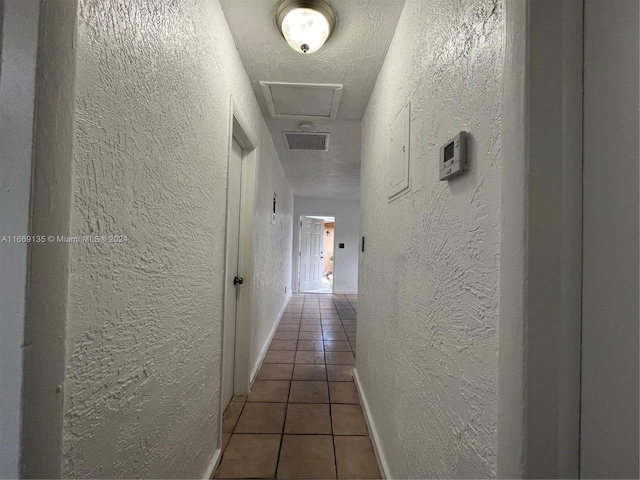 hallway with visible vents, attic access, a textured wall, and tile patterned floors