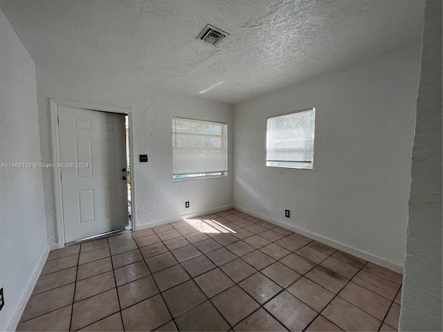 tiled spare room with visible vents, a textured ceiling, and a textured wall